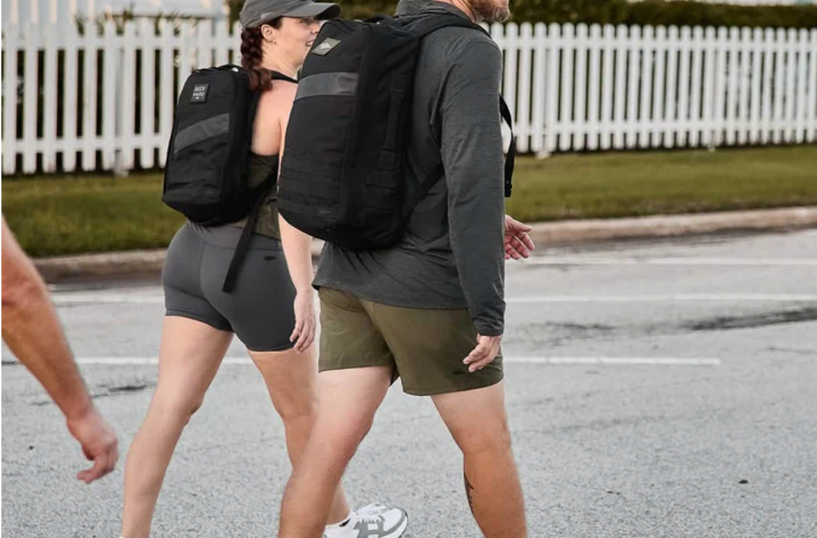 Two people walking down a street wearing backpacks.